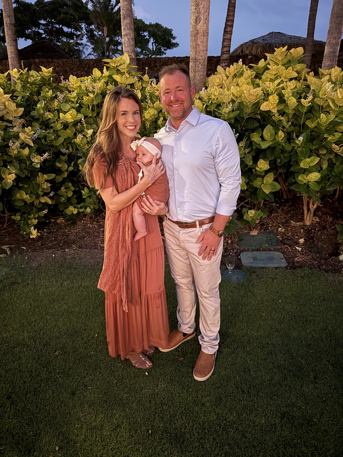 Preston Schrader with his wife and infant daughter at sunset, surrounded by tropical greenery.